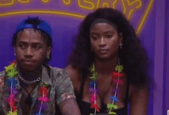 a man and a woman are sitting next to each other . the woman is wearing a lei around her neck .