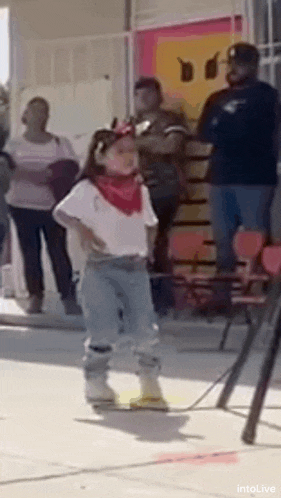 a little girl is dancing in front of a crowd of people while wearing a red bandana .