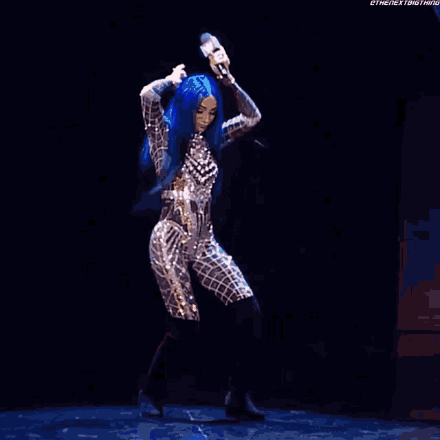 a woman with blue hair is holding a microphone and dancing on stage .