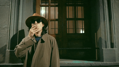 a man in a hat smoking a cigarette in front of a door