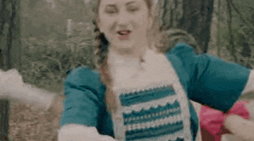 a woman in a blue and white dress is dancing in the woods with her arms outstretched .