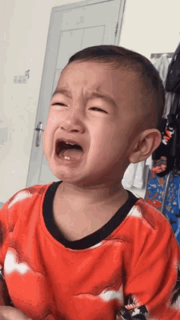 a baby is crying with his mouth open and wearing a red shirt