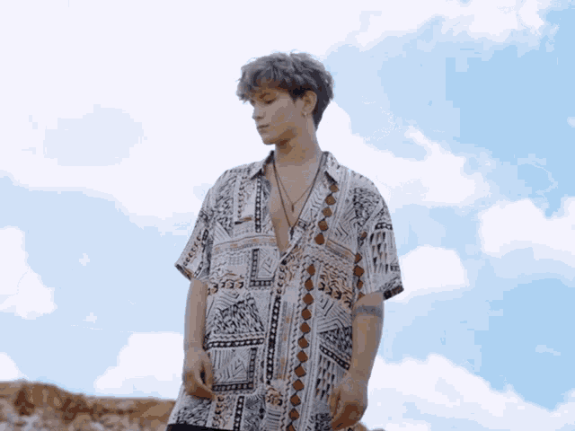 a young man wearing a shirt with a geometric pattern stands in front of a blue sky