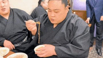 a man in a black kimono is eating noodles from a bowl