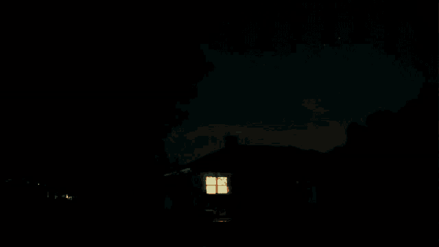 a house is lit up at night with a car driving by