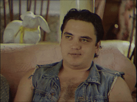 a man in a denim vest is sitting on a couch with his hand on his mouth .