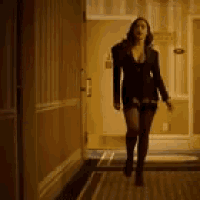 a woman is walking down a hallway with a door in the background .