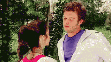 a man and a woman are looking at each other with trees in the background .