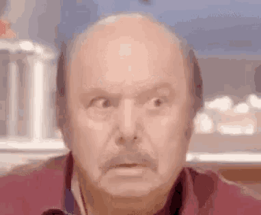 an old bald man with a mustache is making a funny face .
