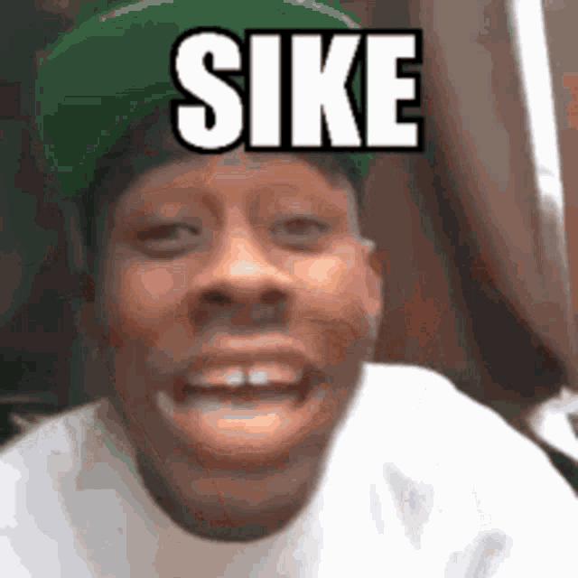 a man wearing a green hat and a white shirt is making a funny face and says sike .