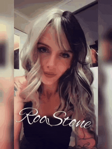 a woman with half black and half white hair is wearing a black top with the word roo stone written on it .