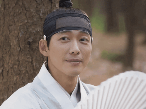 a man wearing a headband and holding a fan looks at the camera