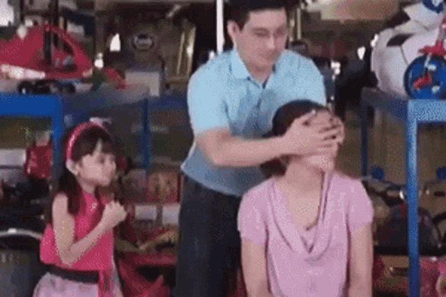 a man is covering a woman 's face while a little girl watches .