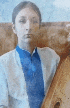 a young girl in a blue and white shirt and tie is holding a wooden instrument .