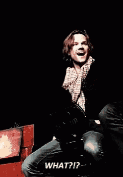 a man is sitting on a chair with his arms outstretched and a microphone in his hand .