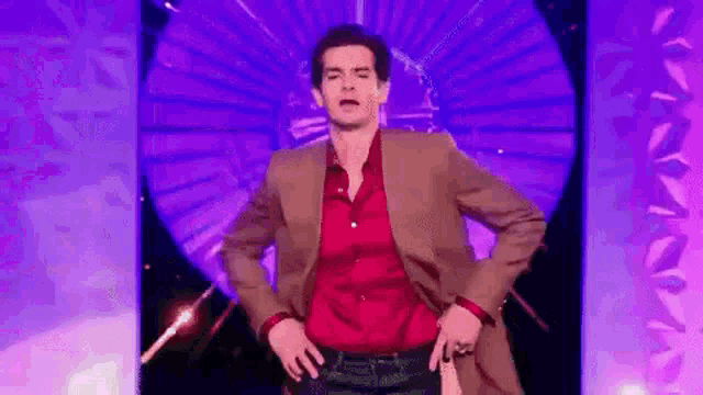 a man in a suit and red shirt is dancing on a stage with a purple background .