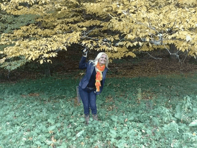 a woman in an orange scarf is standing in the grass near a tree with yellow leaves