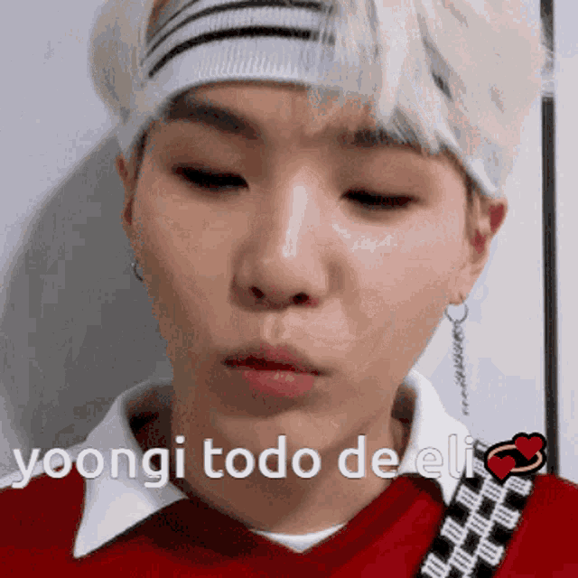 a young man wearing a red shirt and a headband with the words " yoongi todo de eli " on the bottom