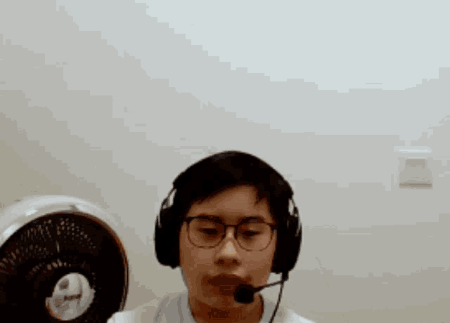 a man wearing headphones and a microphone with a fan behind him