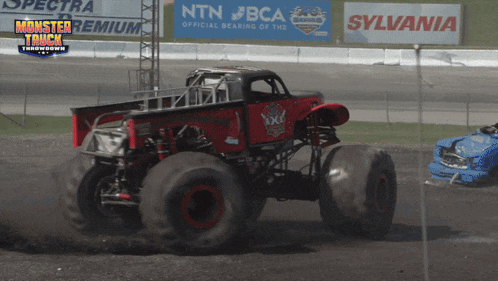 a monster truck is driving down a dirt road with a sylvania sign in the background