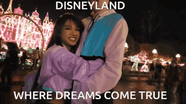 a man and a woman are hugging in front of a disneyland sign