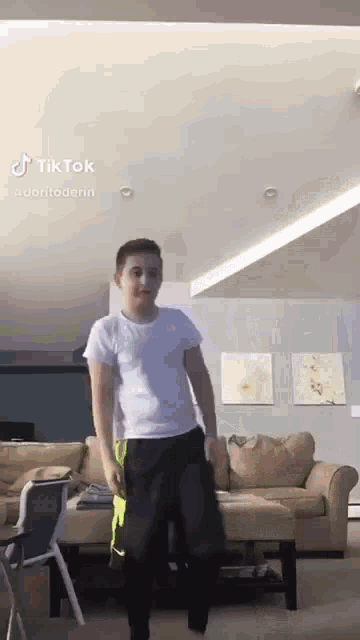 a young man is dancing in a living room with a couch and ottoman .