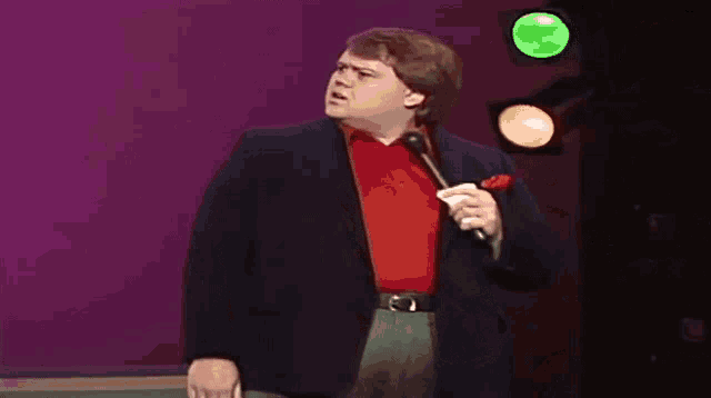 a man in a suit is singing into a microphone on a stage with a green light behind him