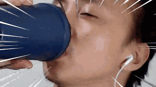 a man drinking from a blue cup with ear buds in his ears