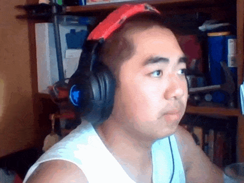 a man wearing headphones and a red hat is sitting in front of a bookshelf .