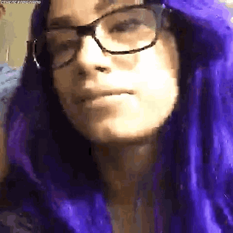 a woman with purple hair and glasses is wearing a purple wig .
