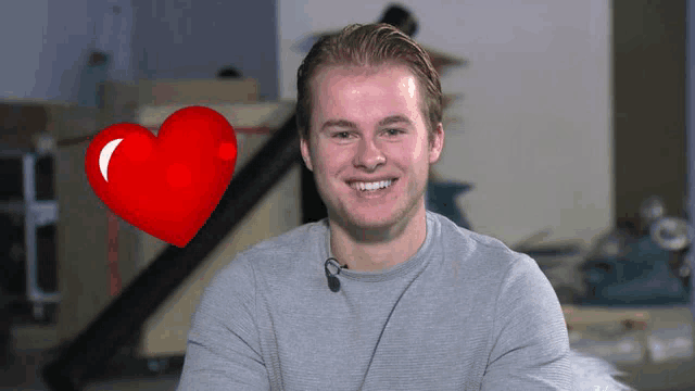 a man smiles with a red heart in the background