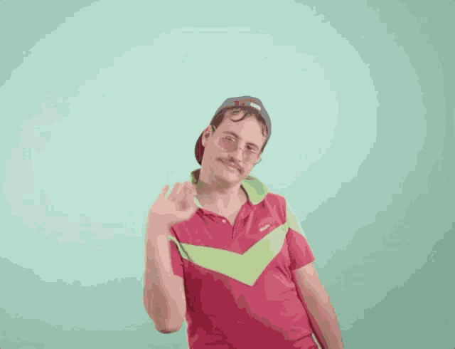 a man with a mustache and glasses is wearing a hat and waving at the camera .