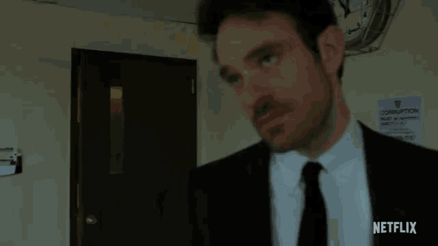 a man in a suit and tie is standing in a room with a sign that says corruption next to him