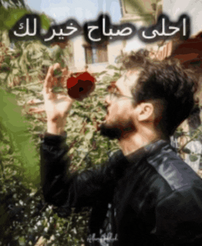 a man in a black jacket is holding a red apple in his hand with arabic writing behind him