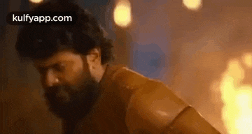 a man with a beard is standing in front of a fire in a room .
