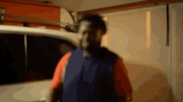 a man in a blue vest is standing in a garage next to a car .