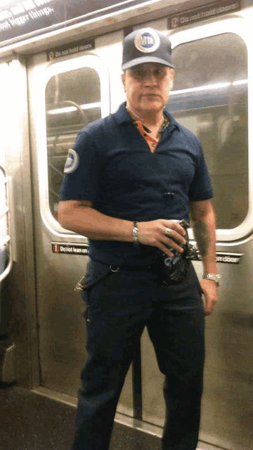 a man in a blue shirt and hat stands in front of a door that says do not hold doors