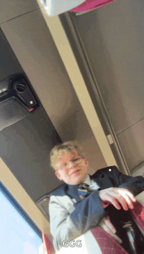 a boy in a suit and tie sits on a bus with ggg written on the bottom of the photo