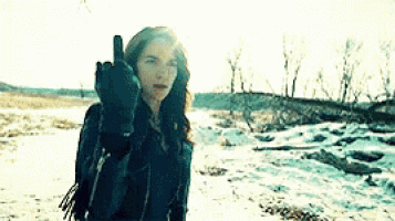 a woman in a black jacket and gloves is giving the middle finger in the snow .