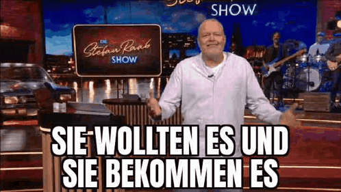 a man is standing on a stage in front of a sign that says `` sie wollten es und sie kommen es '' .