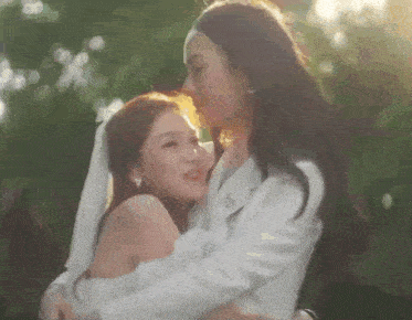 two women in white dresses are hugging each other in a park .