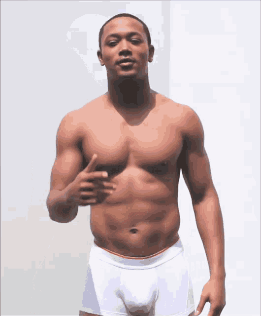 a shirtless man in white boxer briefs is standing in front of a white wall