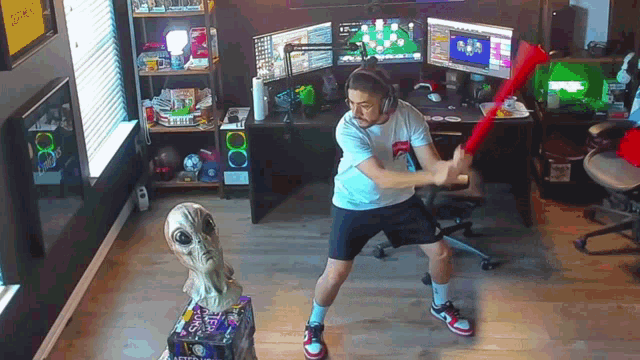 a man playing a video game in a room with a statue of an alien behind him