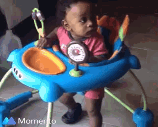 a baby in a blue and orange walker with the word momento on the bottom right
