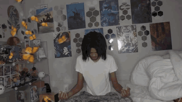 a man sits on a bed in front of a wall that has posters on it including one that says ' samurai '