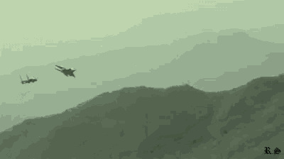 two fighter jets are flying over a mountain range in a foggy sky .