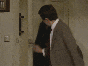 a man in a suit and tie is standing in a room with boxes and a large clock