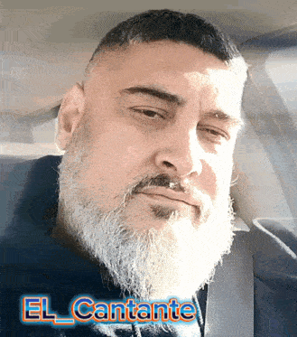 a man with a beard is sitting in a car with the name el cantante on the bottom