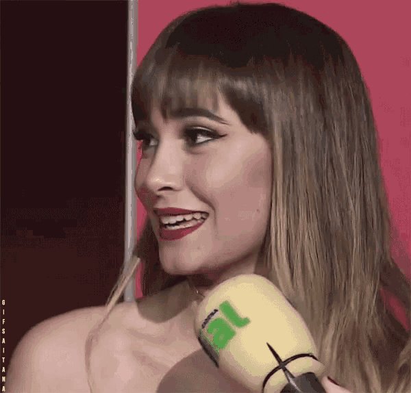 a woman is smiling while holding a yellow microphone with the letter l on the top