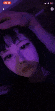 a girl is taking a selfie in the dark with a purple light behind her .